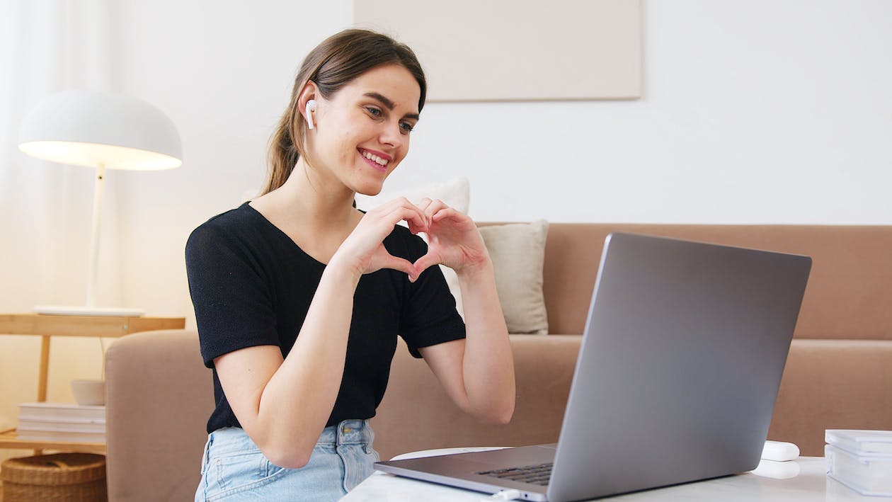 Une femme fait un cœur avec ses mains devant un ordinateur portable
